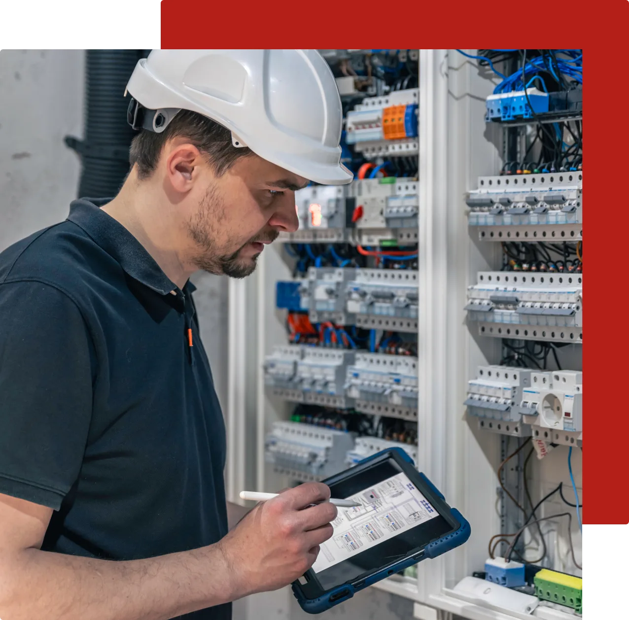 Engineer in a hard hat using a tablet to assess a complex electrical panel, demonstrating expertise in partial discharge detection and system monitoring in an industrial setting.